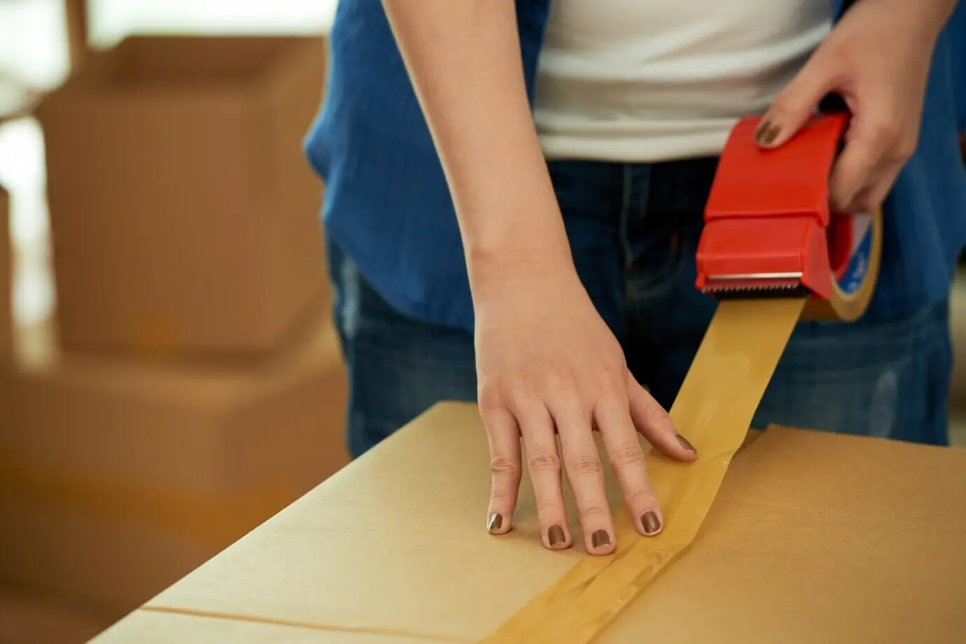 Cropped shot of an unrecognizable woman packing a box with an adhesive tape dispenser.