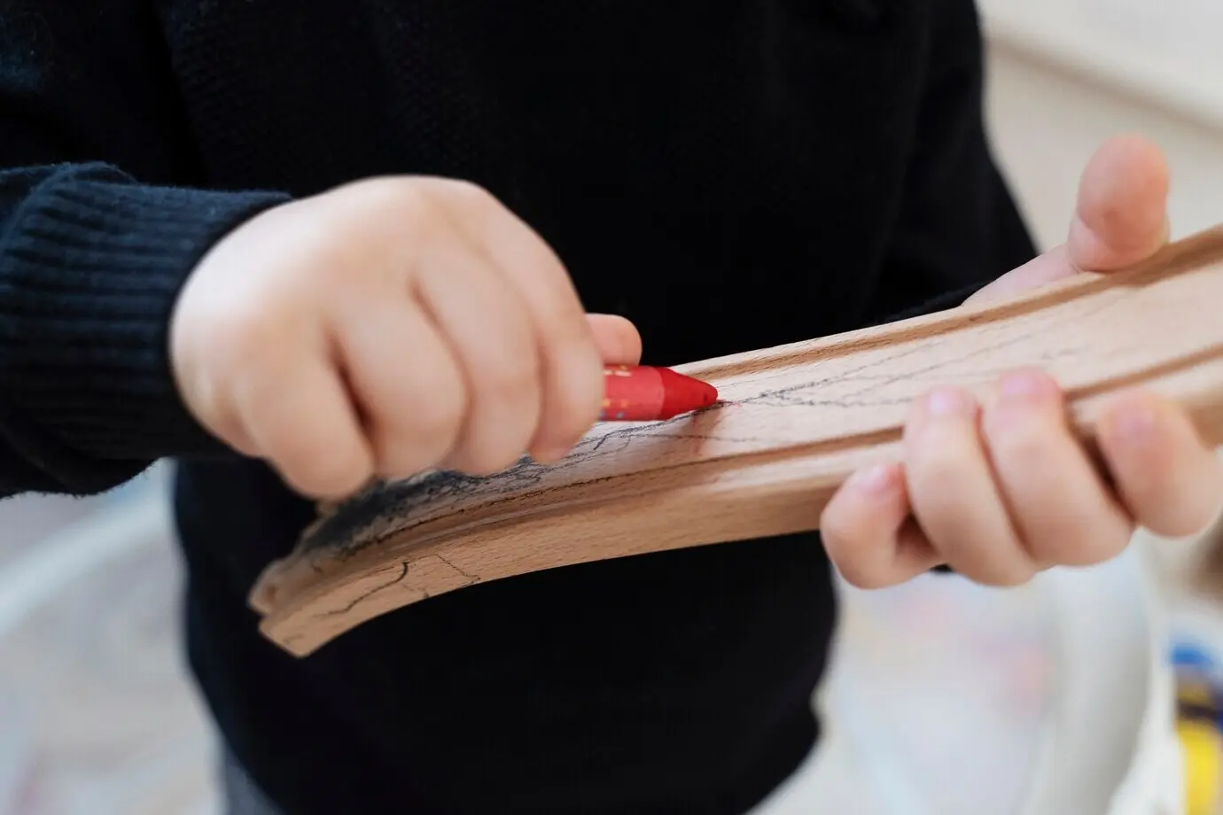 Close-up of a kid drawing on a wooden piece.